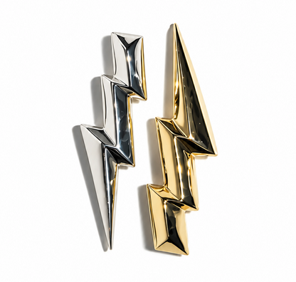 Two metallic lightning bolpendants, one polished silver and one polished gold, displayed on a clean white background.